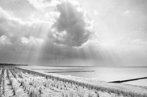 Sun rays shining through dense clouds on the beach of the Baltic Sea. black and white