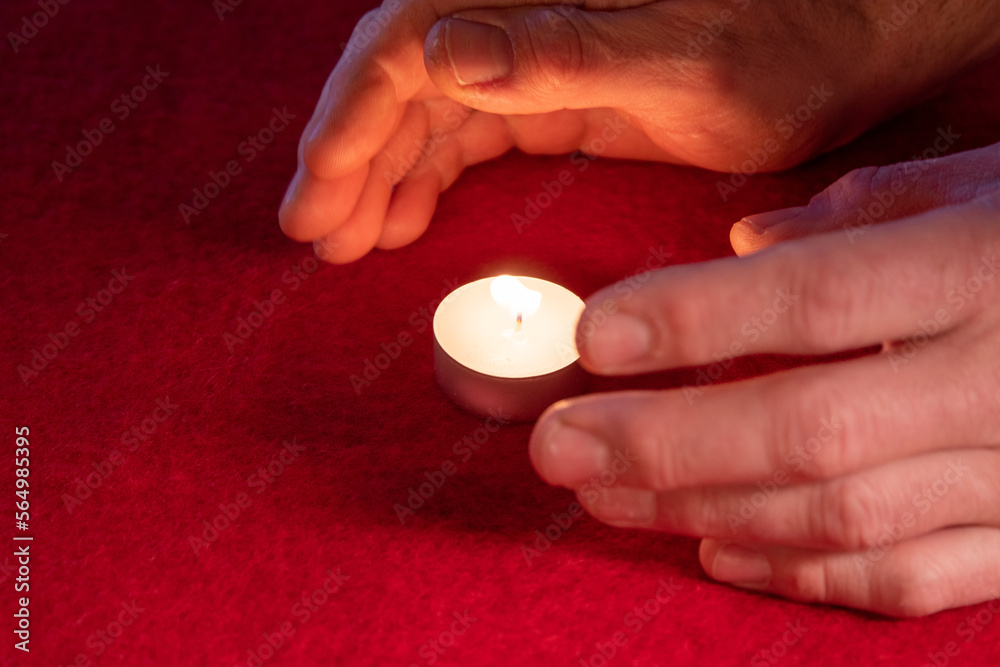 Hands warming themselves on a tealight, red background Hands warming themselves on a tealight, red background