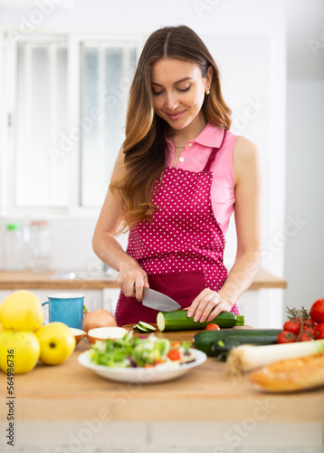 Portrait of woman standing at kitchen table at home  slicing vegetables  cooking salad