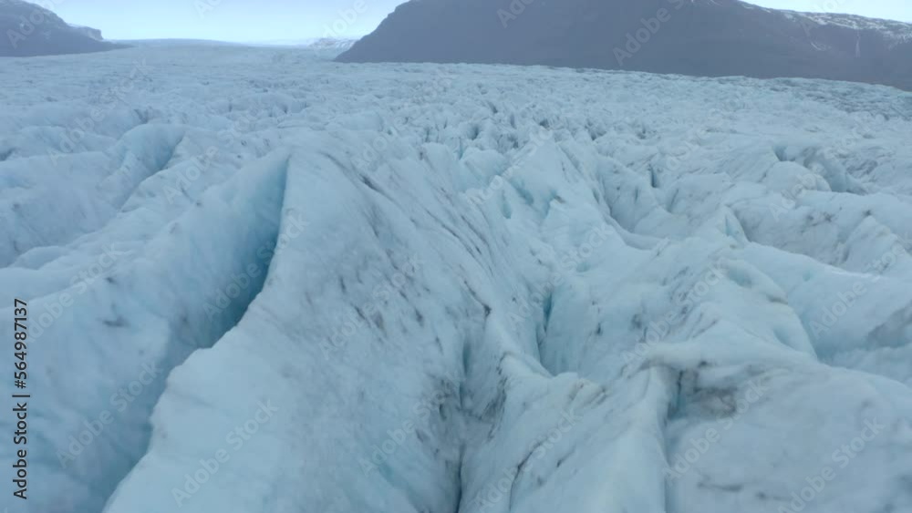 Low cinematic aerial shot over cracks and ridges in a large glacier Low cinematic aerial shot over cracks and ridges in a large glacier
