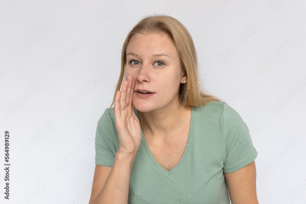 Secretive young woman whispering. Portrait of pleased Caucasian female model with fair hair in green T-shirt looking at camera, telling secret with hand near mouth. Gossip, announcement concept Secretive young woman whispering. Portrait of pleased Caucasian female model with fair hair in green T-shirt looking at camera, telling secret with hand near mouth. Gossip, announcement concept