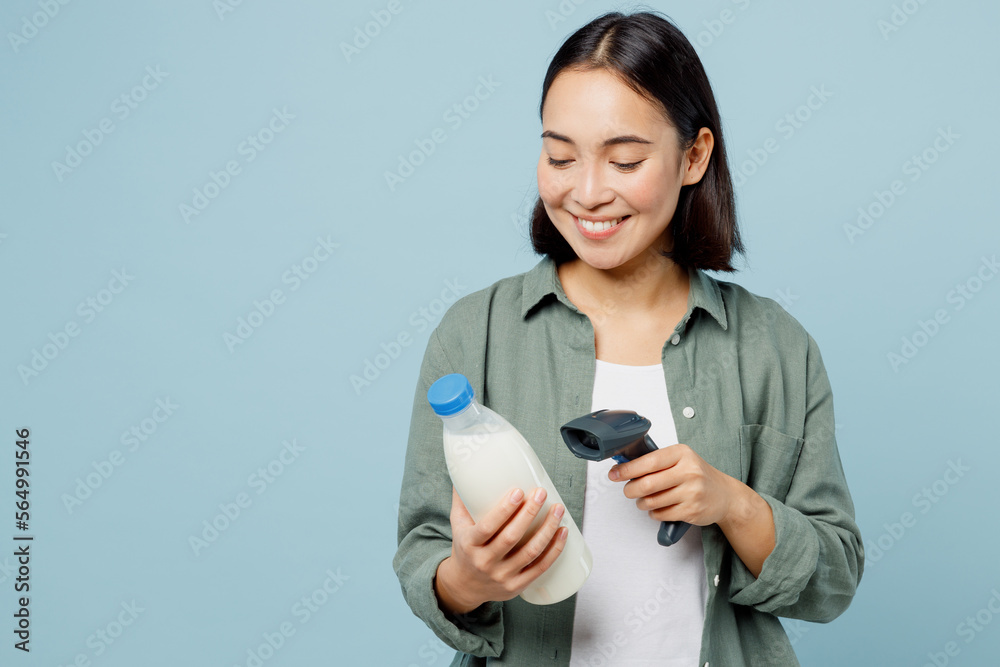 Young smiling happy cheerful woman wear casual clothes holdin hand bottle of milk scanning check bar code isolated on plain blue background studio portrait. Delivery service from shop or restaurant. Young smiling happy cheerful woman wear casual clothes holdin hand bottle of milk scanning check bar code isolated on plain blue background studio portrait. Delivery service from shop or restaurant.