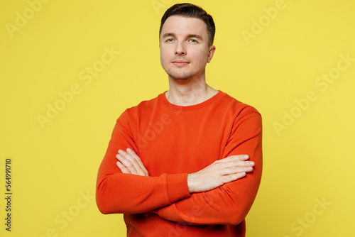 Young calm successful attractive caucasian man wearing orange casual clothes look camera hold hands crossed folded isolated on plain yellow color background studio portrait. People lifestyle concept.