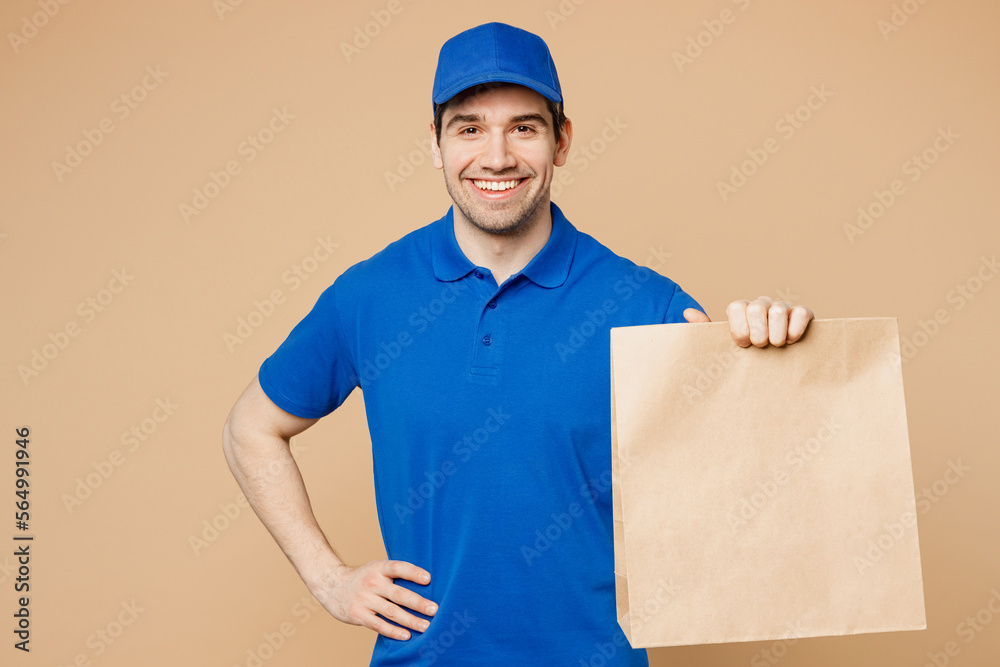 Delivery guy employee man wear blue cap t-shirt uniform workwear work as dealer courier hold brown clear blank craft paper takeaway bag mockup isolated on plain light beige background Service concept Delivery guy employee man wear blue cap t-shirt uniform workwear work as dealer courier hold brown clear blank craft paper takeaway bag mockup isolated on plain light beige background Service concept