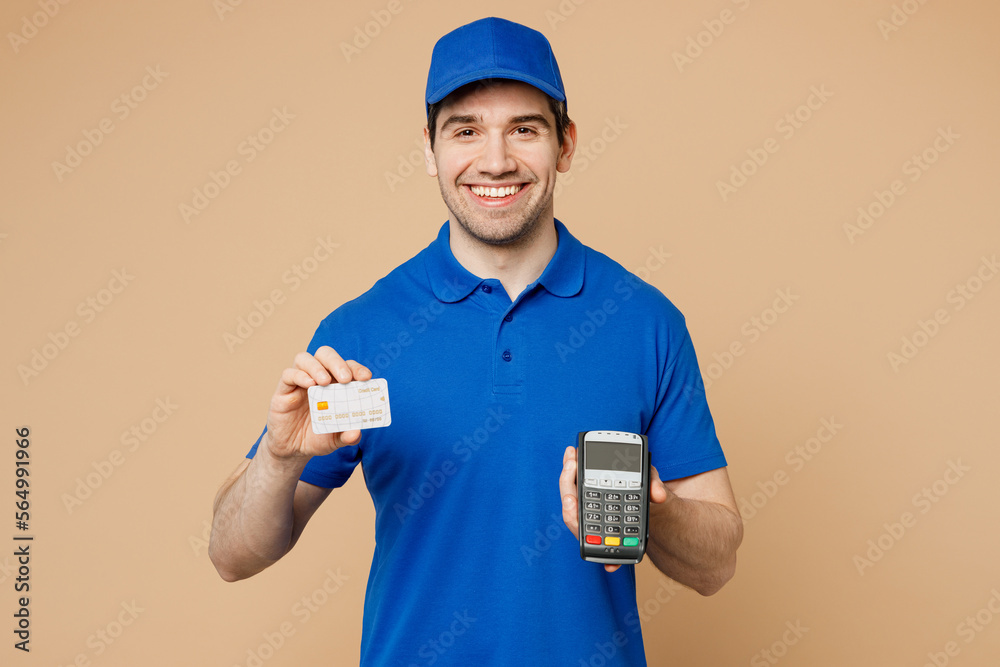 Delivery guy happy employee man wear blue cap t-shirt uniform workwear work as dealer courier hold wireless bank payment terminal process acquire credit card isolated on plain light beige background Delivery guy happy employee man wear blue cap t-shirt uniform workwear work as dealer courier hold wireless bank payment terminal process acquire credit card isolated on plain light beige background