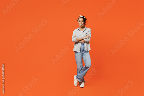 Full body fun young woman of African American ethnicity she wears grey shirt headband lok camera hold hands crossed folded isolated on plain orange background studio portrait People lifestyle concept