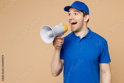 Happy delivery guy employee man wear blue cap t-shirt uniform workwear work as dealer courier hold in hand megaphone scream announces discounts sale Hurry up isolated on plain light beige background.
