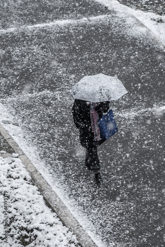People walks on the urban city street on a snowy winter day with small white snow snowflakes in foreground