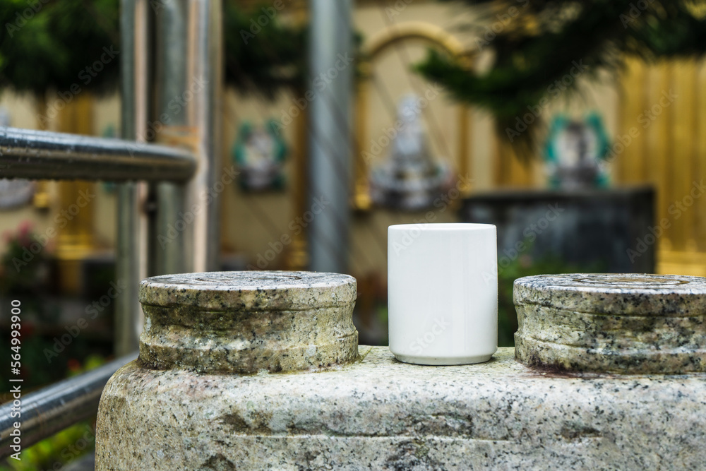 A Coffee mug standing still above a rock fence with out of focus statue carvings