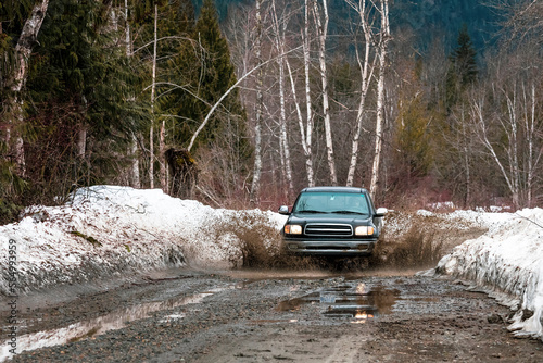 A man drives his pickup truck through a mud puddle on a dirt road. photo