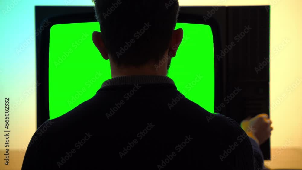 Back view shot of male person sitting in front of vintage TV with blinking green screen chroma key and horizontal stripes, person switching on and off different buttons on TV control panel, television Back view shot of male person sitting in front of vintage TV with blinking green screen chroma key and horizontal stripes, person switching on and off different buttons on TV control panel, television