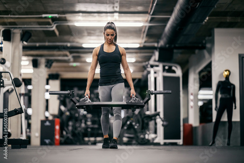 A strong sportswoman is walking and carrying weights in a gym during her strength training.