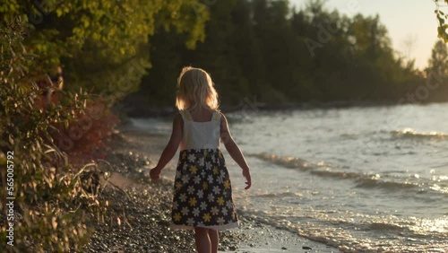 Young Blonde Girl Walking Along Pebble Beach at Sunset