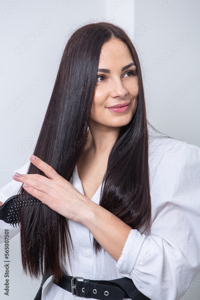 Young woman combing her long dark hair with a comb in a beauty salon , woman's hair in beauty salon, hairstyle concept Young woman combing her long dark hair with a comb in a beauty salon , woman's hair in beauty salon, hairstyle concept