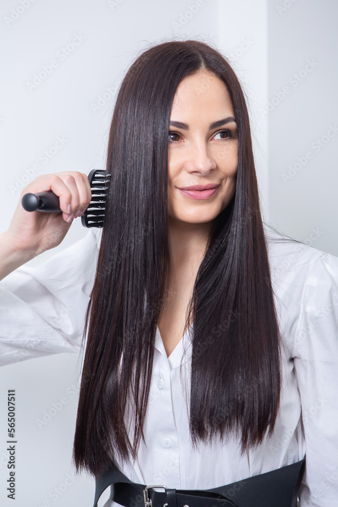 Young woman combing her long dark hair with a comb in a beauty salon , woman's hair in beauty salon, hairstyle concept
