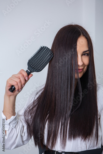 Young woman combing her long dark hair with a comb in a beauty salon , woman's hair in beauty salon, hairstyle concept