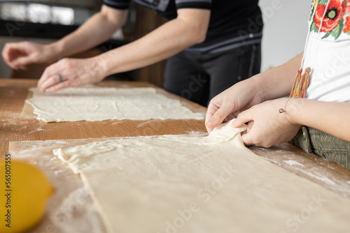 Mother and daughter spread the dough on the kitchen table for further baking