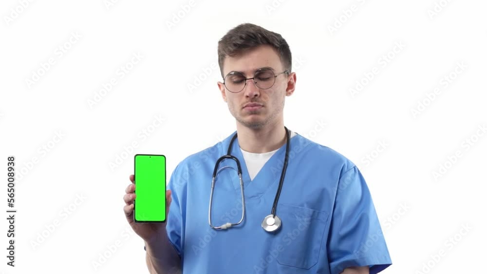 Doctor nurse in uniform and with a stethoscope points to a smartphone with a green screen advertising medical pharmacology and concept of modern medicine. Smiling on a white background. Doctor nurse in uniform and with a stethoscope points to a smartphone with a green screen advertising medical pharmacology and concept of modern medicine. Smiling on a white background.