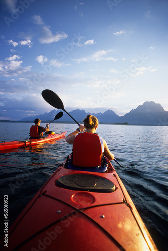 A young couple paddles sea kayaks across Jackson Lake on a sunny day in Grand Teton National Park, Jackson Hole, Wyoming.