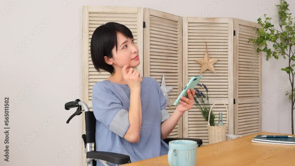 家でスマホでを持って想像する車椅子に乗った障がい者女性 家でスマホでを持って想像する車椅子に乗った障がい者女性