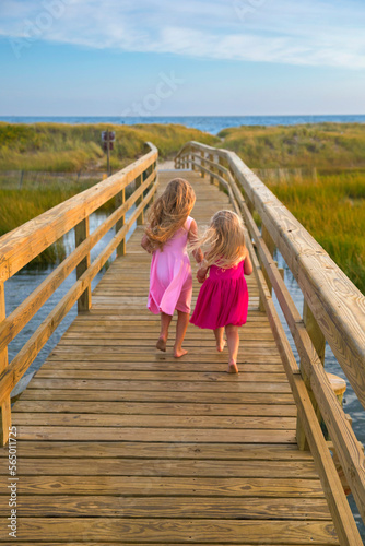 Little Girls From Behind Running On Bridge to Beach in Pink Dresses