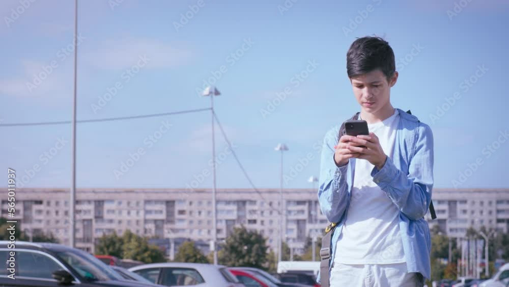 teen boy uses the phone in the street at sunny day, reads sms, reads correspondence teen boy uses the phone in the street at sunny day, reads sms, reads correspondence