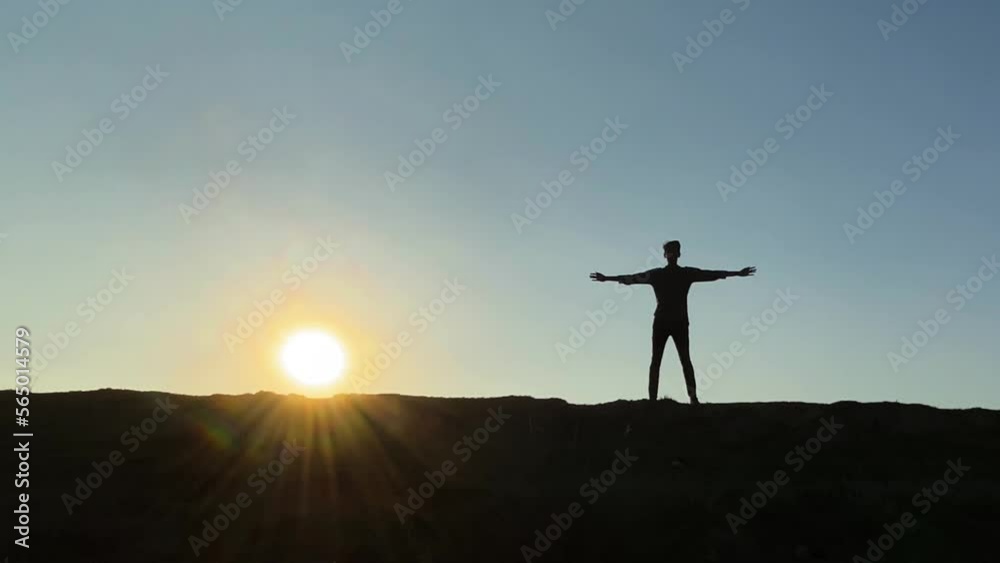 Silhouetted man rises arms, doing exercise, tired after run, bright sunset behind