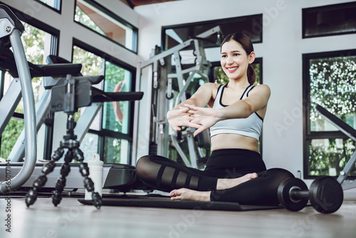Asian woman training exercise on yoga mat and using mobile phone. Female sport blogger recording video by smart phone. Exercise online training class at gym indoors.