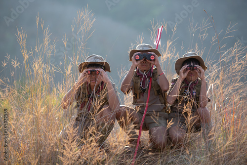 Three boy scouts exploring nature with binoculars in camp photo