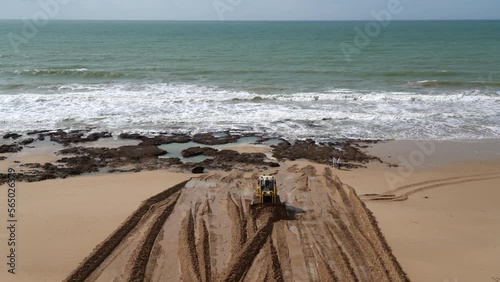 Tractor bulldozer on the sea beach levels and raises the shoreline with sand after washing out.