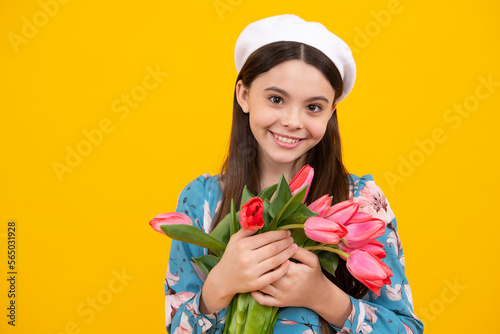 Beautiful smiling trendy teen girl with bouquet of tulips on yellow studio background. Girl enjoying flowers.