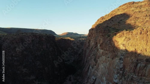Cinematic aerial view dolly flying over a lush desert gorge between two cliffs at golden hour at riemvasmaak park in south africa near namibia. Drone Flight Through a Wild Desert Landscape