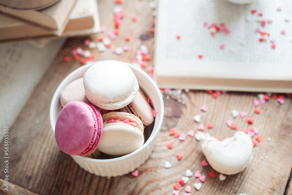 Macaroons in a bowl on a book background of small hearts on a wooden background,top view Macaroons in a bowl on a book background of small hearts on a wooden background,top view