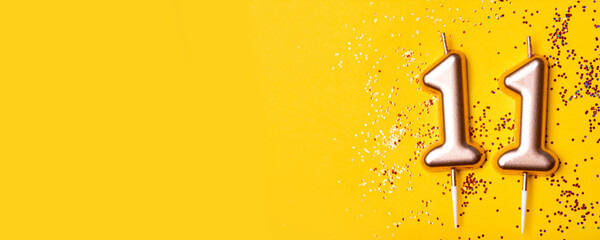 Gold candles in the form of number eleven on yellow background with confetti. 11 years celebration.