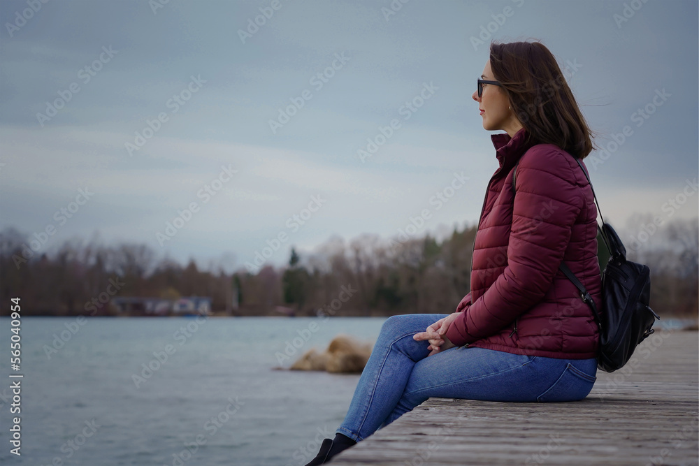 The girl sits on a wooden bridge near the lake and looks into the distance.