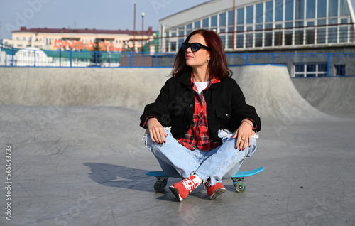 An active middle-aged woman rides a skateboard on an empty road or highway. An ordinary city woman relaxing on a skateboard after work. The concept of a modern lifestyle