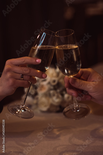 Two glasses with sparkling champagne wine in hands, concept for holiday, bokeh, in a restaurant. Romantic dinner. Man and woman are holding glasses of champagne. Concept for Valentine's day or date