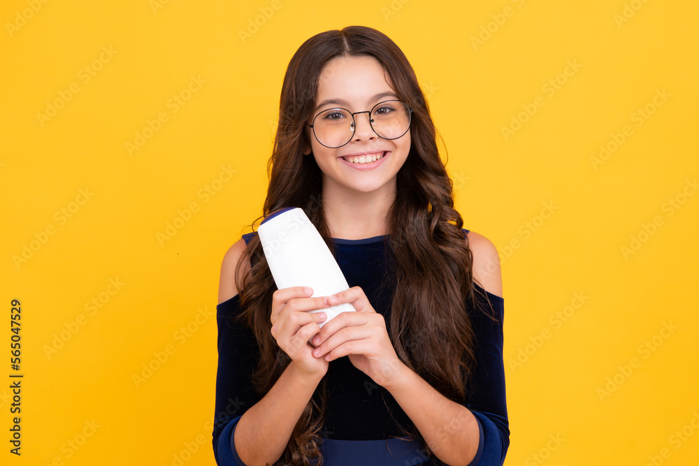 Teen child girl with shampoo bottle or shower gel isolated on yellow background. Kids hair cosmetic product. Happy face, positive and smiling emotions of teenager girl. Teen child girl with shampoo bottle or shower gel isolated on yellow background. Kids hair cosmetic product. Happy face, positive and smiling emotions of teenager girl.