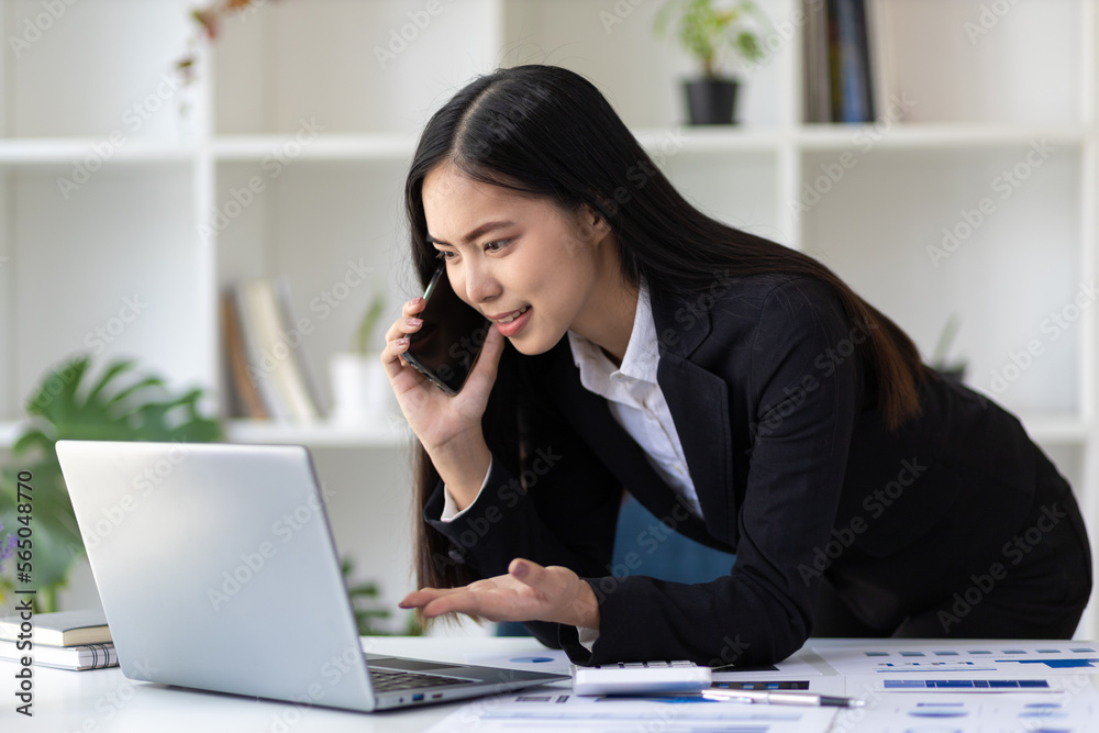 Businesswoman working with documents on laptop in office. The secretary is talking on the mobile phone and analyzing the monthly work schedule. Businesswoman working with documents on laptop in office. The secretary is talking on the mobile phone and analyzing the monthly work schedule.