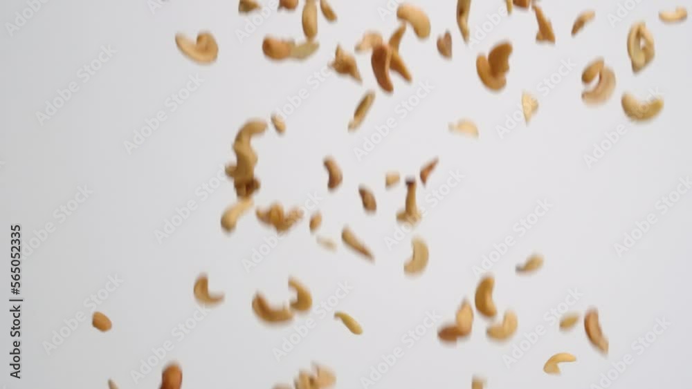 Roasted and salted cashew halves falling in slow motion on white backdrop Roasted and salted cashew halves falling in slow motion on white backdrop