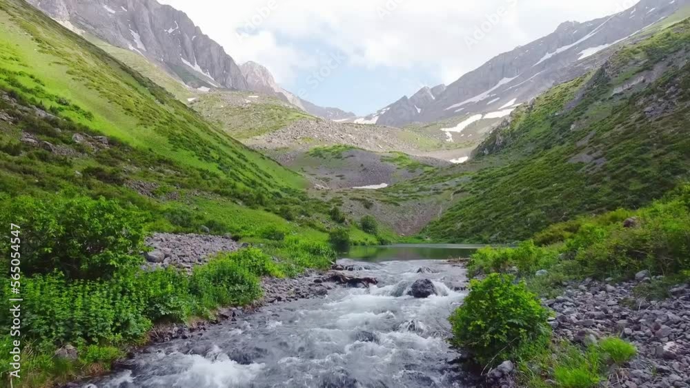 The drone flies over a transparent mountain river in the highlands. High in the mountains in a canyon with different vegetation and stones a mountain river flows. The drone flies over a transparent mountain river in the highlands. High in the mountains in a canyon with different vegetation and stones a mountain river flows.