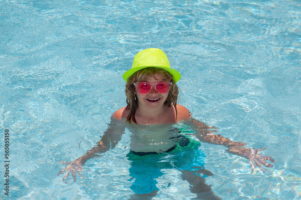 Fashion summer kids in hat and pink sunglasses. Child splashing in swimming pool.