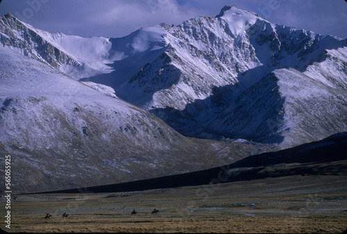 Kyrgyz horsemen ride below snow covered peaks of the Wakhan range, in the Big Pamirs, Wakhan Corridor, Badakshan photo
