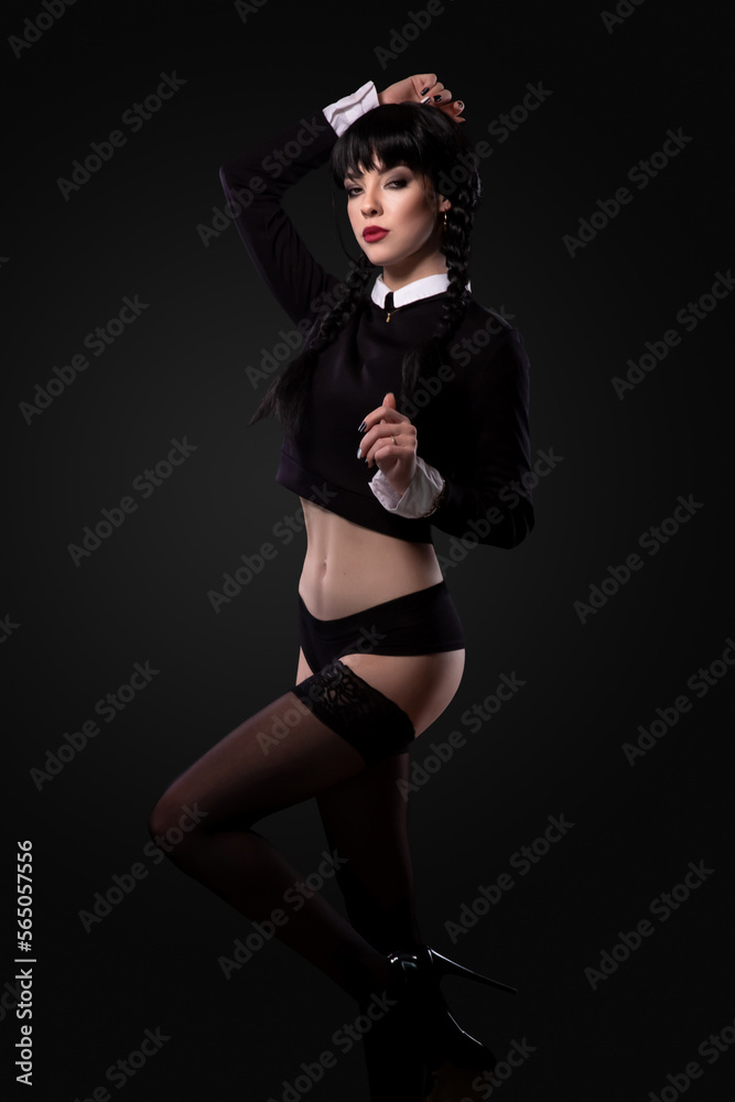 Portrait of a young sexy slim brunette caucasian girl with 2 pigtails standing and attractively posing on a radial gradient grey and black background