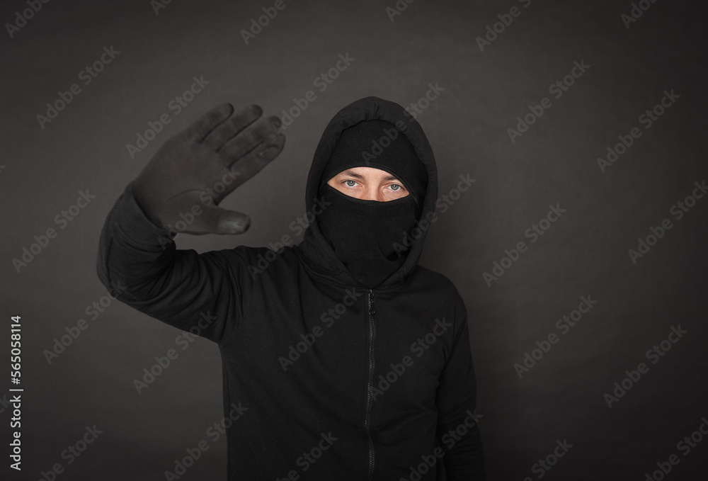 Unrecognizable man in the black hoody with hood wearing balaclava mask holding hand up Unrecognizable man in the black hoody with hood wearing balaclava mask holding hand up
