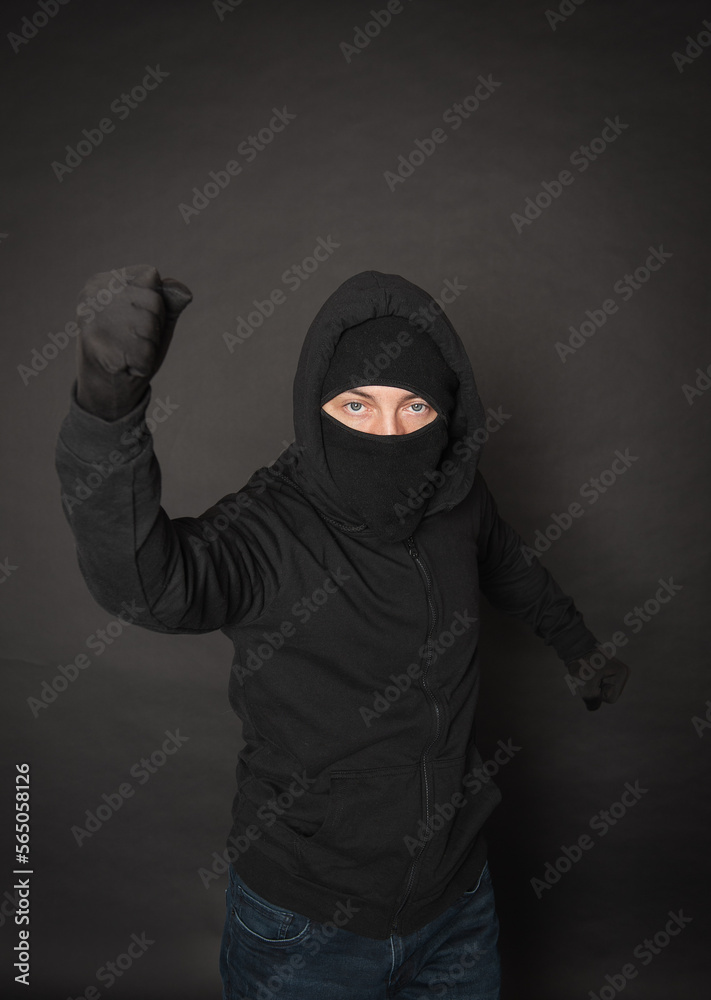 Man in the black hoody with hood wearing balaclava mask with fist up Man in the black hoody with hood wearing balaclava mask with fist up