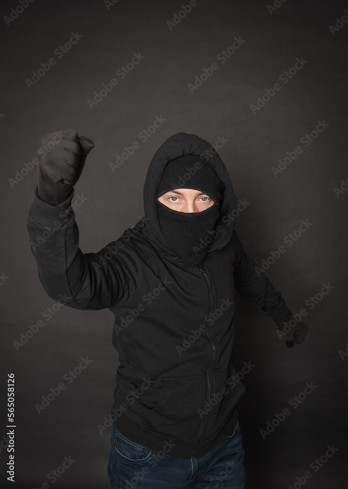 Man in the black hoody with hood wearing balaclava mask with fist up