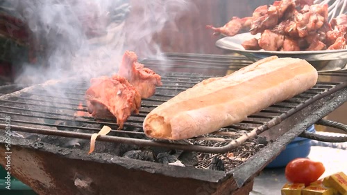 Baguette and chicken meat pieces are frying on a charcoal grill. Close-up of hands twirling food.