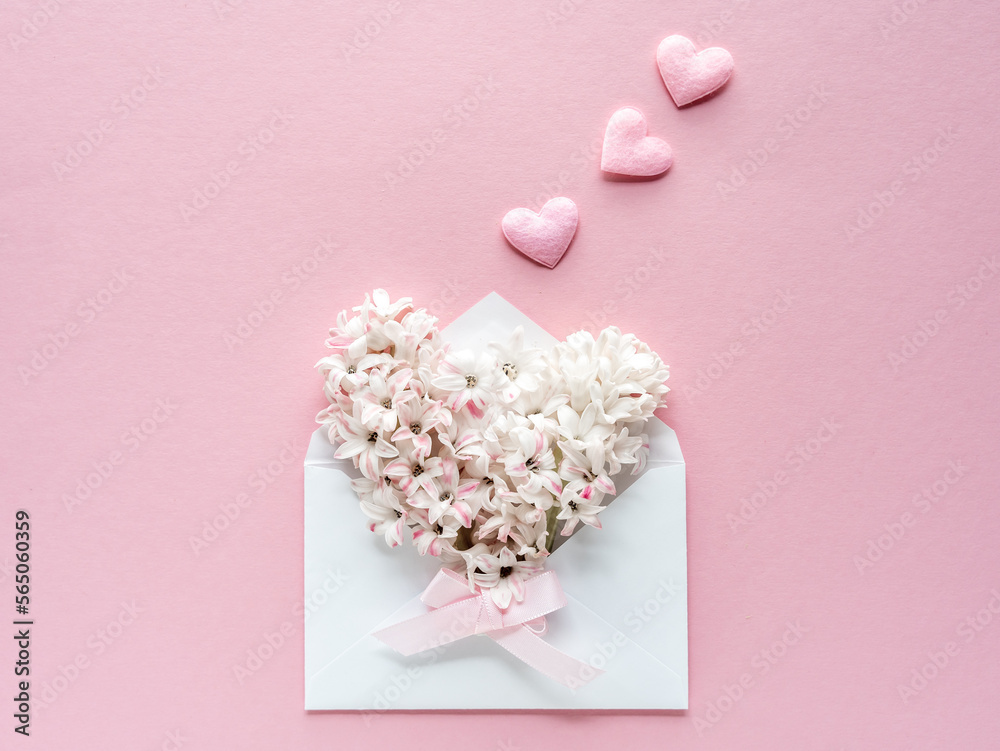 Ein Briefkuvert gefüllt mit weißen Blüten und Herzen auf einem rosa Hintergrund. Grußkarte.