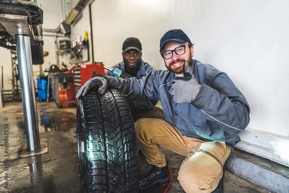 A smiling car mechanic working in a garage changing a car's wheels makes thumbs sign. High-quality photo